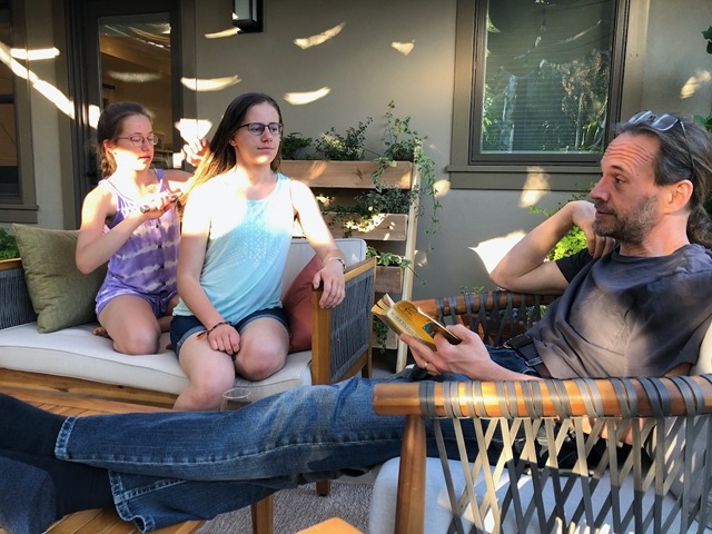 Mike reading The Hobbit for family time, while Ellie braids Lela's hair